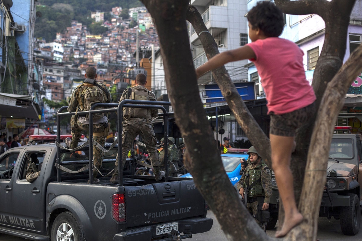 A child climbs a tree as PM militarized police personnel patrol the main street of Rocinha favela in Rio de Janeiro, Brazil on September 28, 2017.