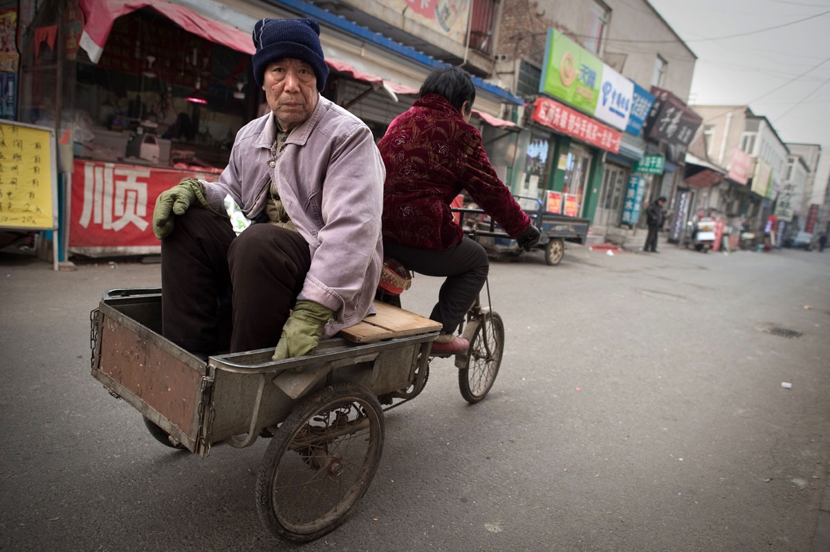 This picture taken on February 15, 2017 shows an elderly man sitting on the back of a tricycle ridden by an elderly woman in the Heiqiaocun migrant village in Beijing.