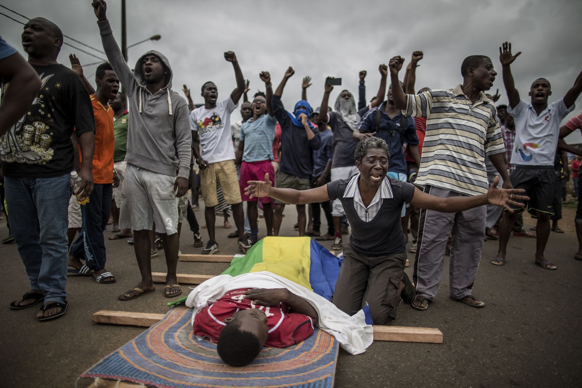 A woman cries over the body of Axel Messa, 30, wrapped in the flag of Gabon as he is laying on the ground, prior to a funeral procession, in a street of the Libreville district of Nzeng Ayong on September 2, 2016. His mother told AFP he was shot in front 