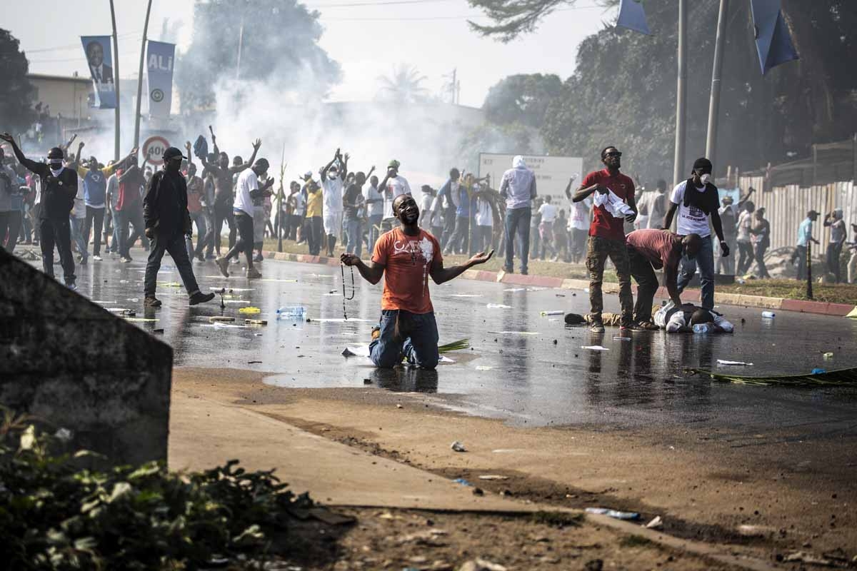 A supporter of Gabonese opposition leader Jean Ping prays in front of security forces blocking a demonstration trying to reach the electoral commission in Libreville on August 31, 2016 as another protestor lays on the ground in distress.