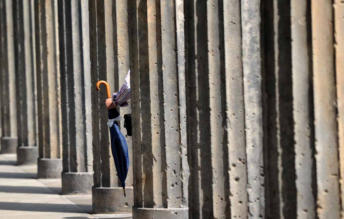 A man carries an umbrella as he walks past columns on the museum island on August 2, 2010 in Berlin. Weahter was unsettled with sinking temperatures and rain in the German capital.