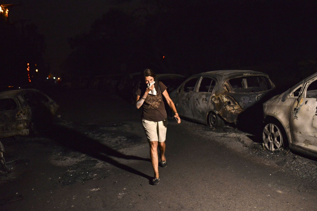 A woman walks in front of burnt cars at the village of Mati during a wildfire near Athens, on July 23, 2018.