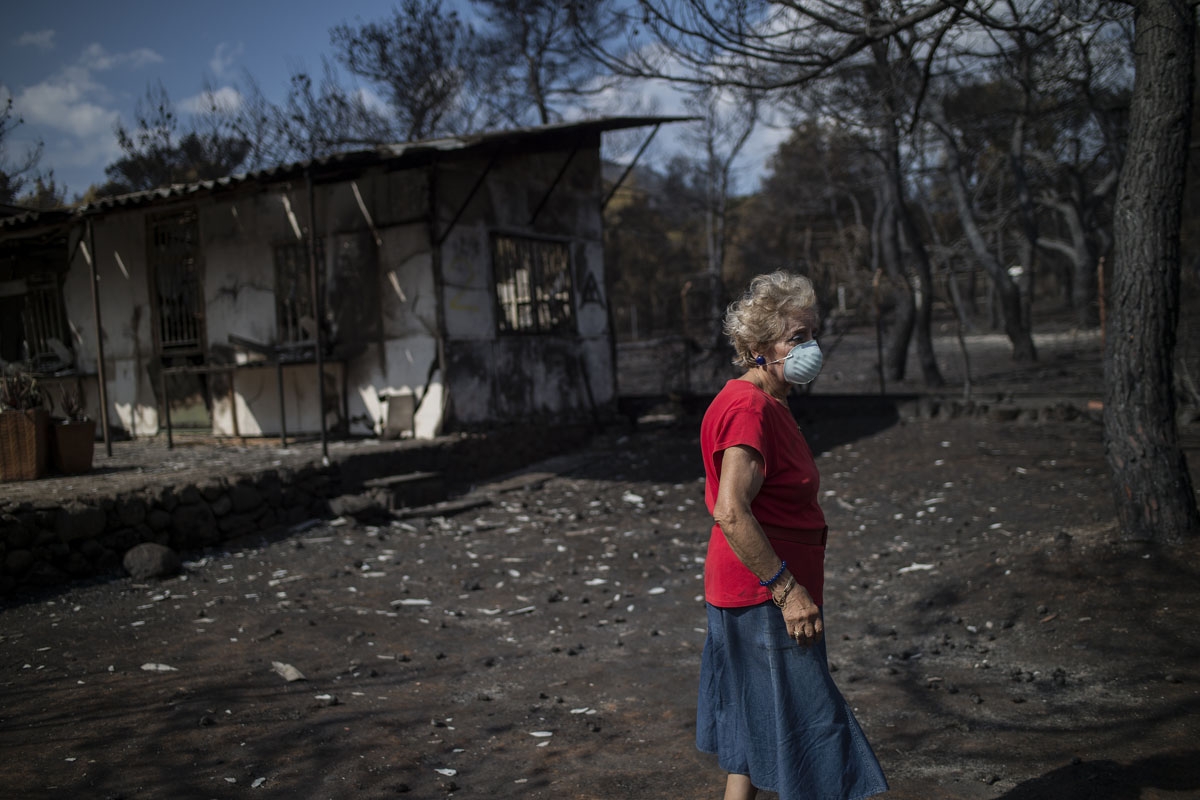 A woman wearing a mask walks in front of her burnt house following a wildfire at the village of Neos Voutzas, near Athens, on July 26, 2018.