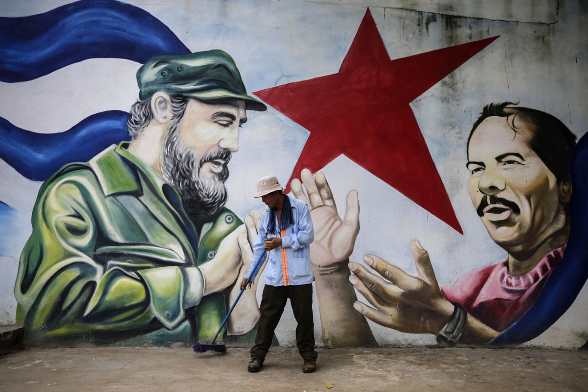 A municipal worker sweeps the floor in front of a mural depicting Cuban revolutionary leader Fidel Castro (L) and Nicaraguan President Daniel Ortega at Cuba square in Managua on November 26, 2016, the day after Castro died.