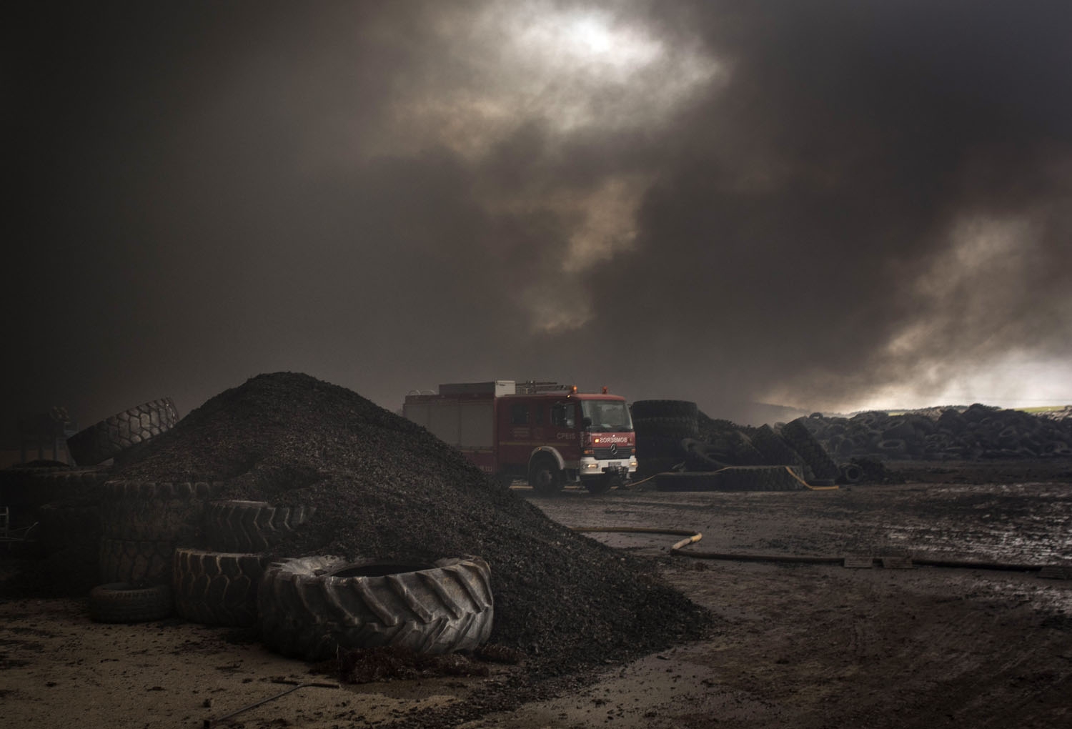 Clouds of dark smoke cover the sky as a fire truck drives among piles of tyres in an uncontrolled dump near the town of Sesena, after a fire brokeout early on May 13, 2016 Clouds of dark smoke cover the sky as a fire truck drives among piles of tyres in an uncontrolled dump near the town of Sesena, after a fire brokeout early on May 13, 2016