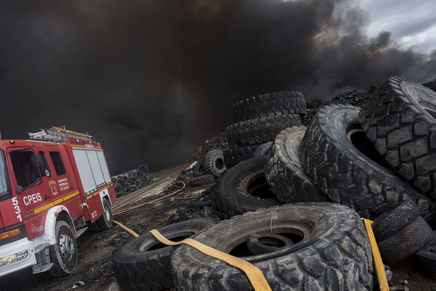 Clouds of dark smoke cover the sky as a fire truck works among piles of tyres in an uncontrolled dump near the town of Sesena, after a fire brokeout early on May 13, 2016 Clouds of dark smoke cover the sky as a fire truck works among piles of tyres in an uncontrolled dump near the town of Sesena, after a fire brokeout early on May 13, 2016