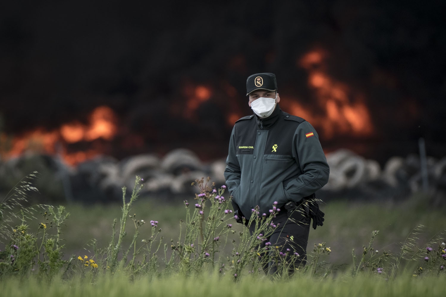 A civil guard with a mask walks past a pile of tyres burning in an uncontrolled dump near the town of Sesena, after a fire brokeout early on May 13, 2016 A civil guard with a mask walks past a pile of tyres burning in an uncontrolled dump near the town of Sesena, after a fire brokeout early on May 13, 2016