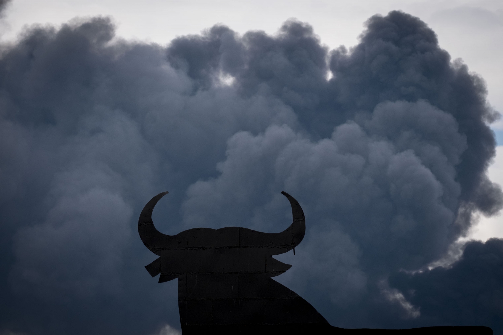 The shape of an Osborne Bull is pictured with black clouds of smoke on the background, produced by tyres burning in an uncontrolled dump near the town of Sesena, after a fire brokeout early on May 13, 2016 The shape of an Osborne Bull is pictured with black clouds of smoke on the background, produced by tyres burning in an uncontrolled dump near the town of Sesena, after a fire brokeout early on May 13, 2016