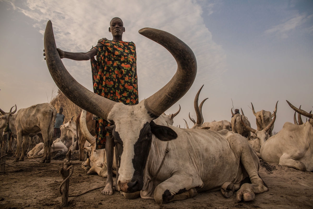 Sudanese girl Den, (14) from Dinka tribe who works as a cattle keeper, cook and cleaner and aid to her brother without attending any school poses at their cattle camp in Mingkaman, Lakes State, South Sudan on March 3, 2018. During South Sudanâs dry sea