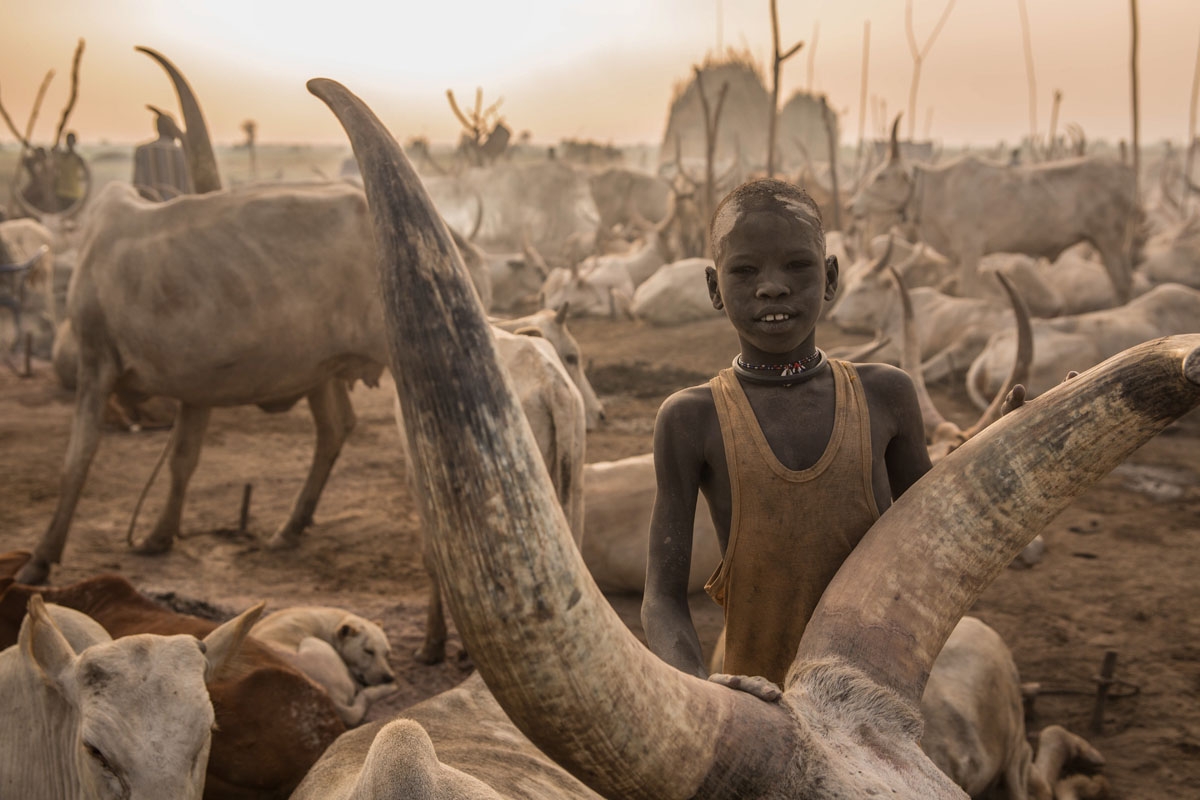 A Sudanese boy from Dinka tribe poses next to his cow at their cattle camp in Mingkaman, Lakes State, South Sudan, on March 3, 2018.