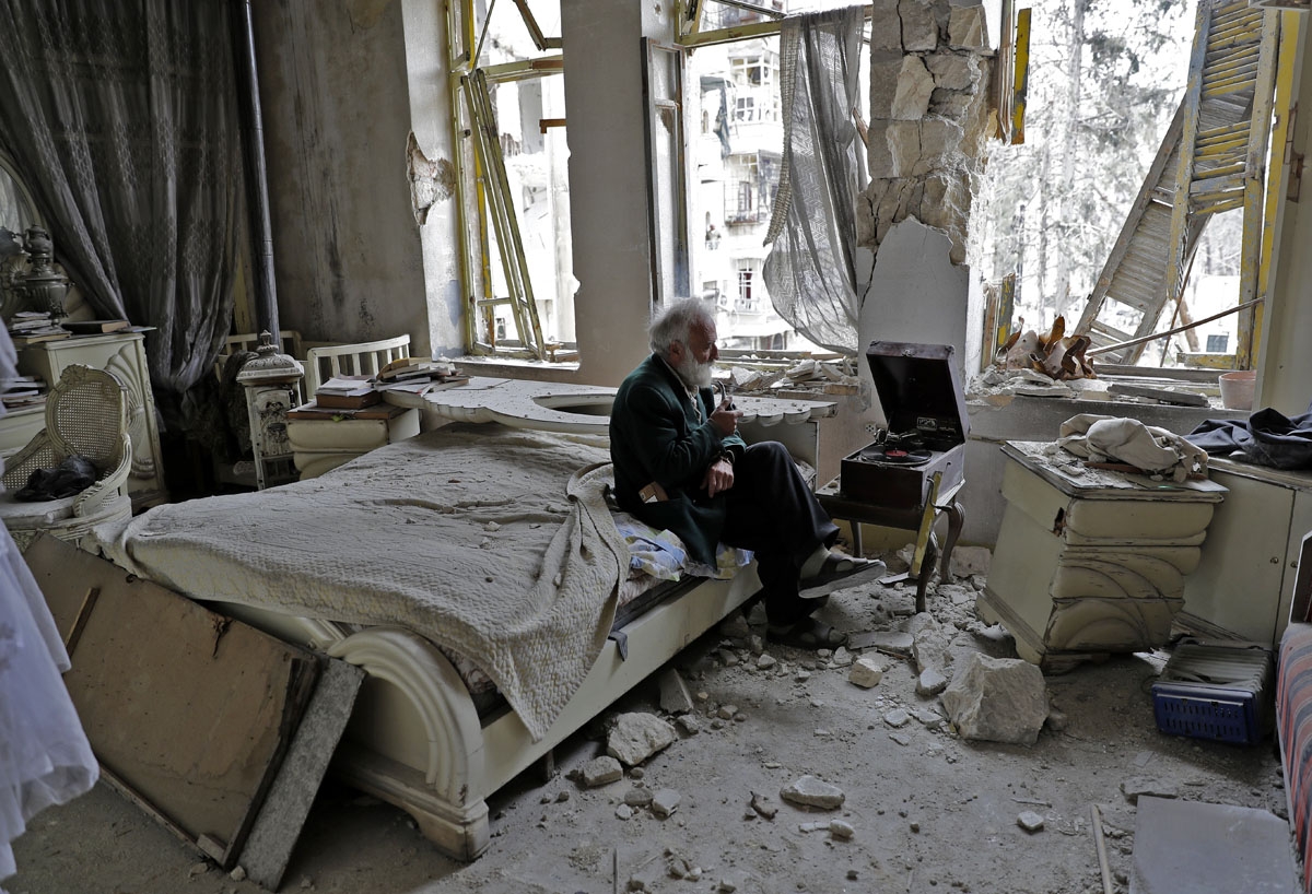 Mohammad Mohiedine Anis, 70, smokes his pipe as he sits in his destroyed bedroom listening to music on his vinyl player, gramophone, in Aleppo's formerly rebel-held al-Shaar neighbourhood.