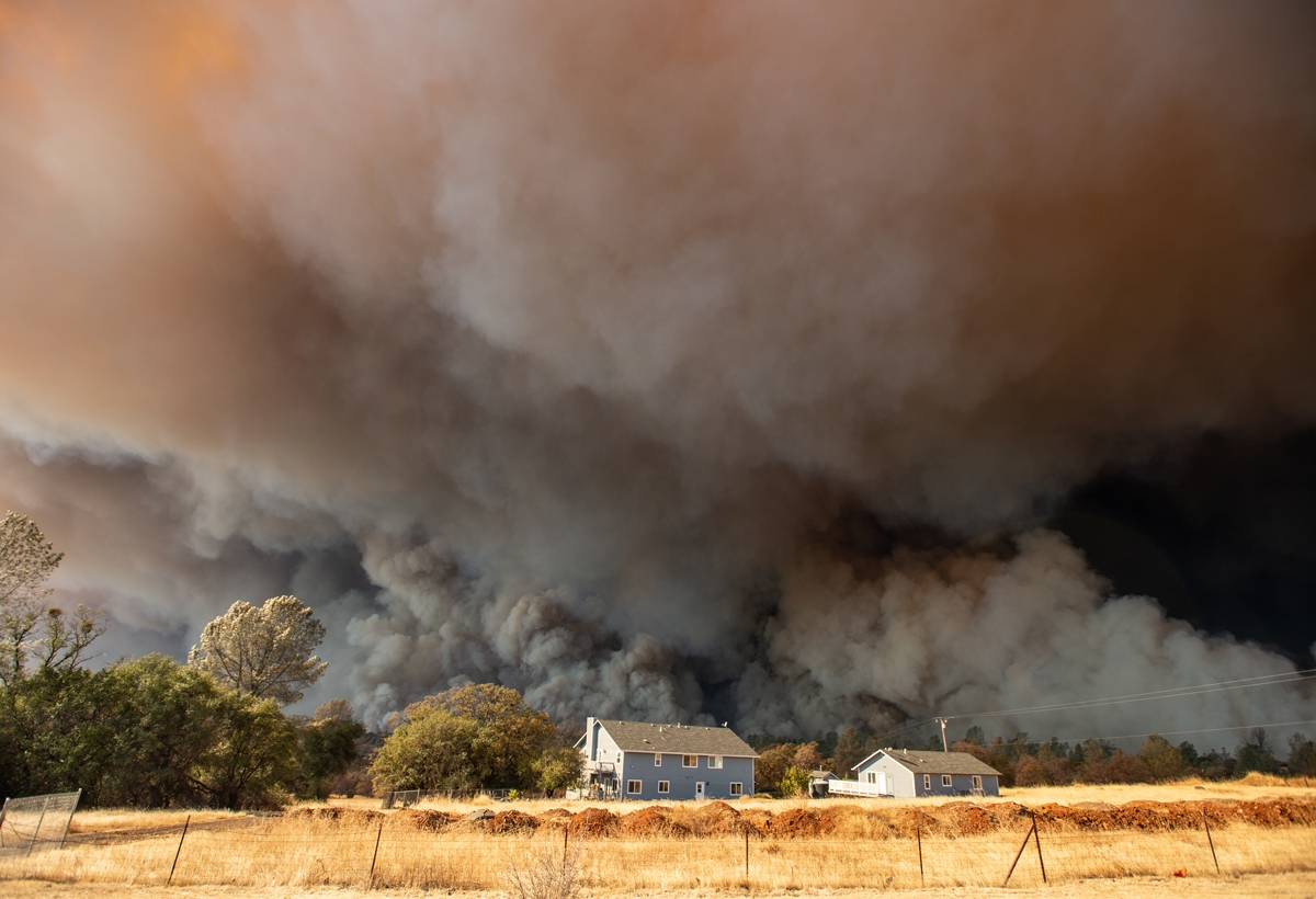 A home is overshadowed by towering smoke plumes as the Camp fire races through town in Paradise, California on November 8, 2018.