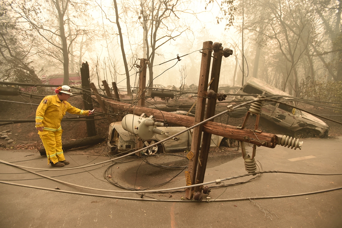 CalFire firefighter Scott Wit surveys burnt out vehicles near a fallen power line on the side of the road after the Camp fire tore through the area in Paradise, California on November 10, 2018.