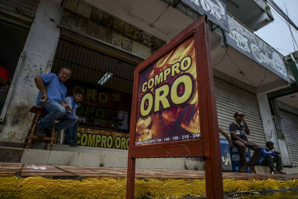 Men sit outside a store reading We buy gold in El Callao, Bolivar state, southeastern Venezuela on February 25, 2017. Although life in the mines of eastern Venezuela is hard and dangerous, tens of thousands from all over the country head for the mines da